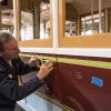 A painter lays down masking tape to paint striping on the side of Powell St. Cable Car 22,