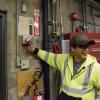 Crew member looking away while holding a wall switch inside a systems shop location.