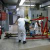 Several crew members holding a large device instrument inside a systems shop location. 