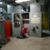 Two crew members in full protected wear inside a shops location. The walls are bordered with systems cabinets and decks. 