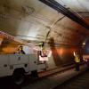 Work trucks along the tunnel wall with a crew member giving directions with their hands. 