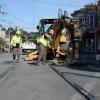 Crew member by the rail track and an excavator with a shovel along the street with houses lined along the side. 