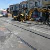 Excavator with extended arm and alongside the rail tracks and residential homes.