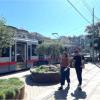 People walking by sidewalk planters near train. 