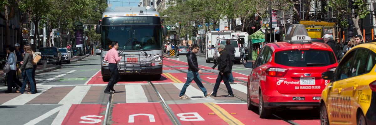 view east on market street with pedestrians, taxis, and Muni bus in street and red transit only lane in foreground