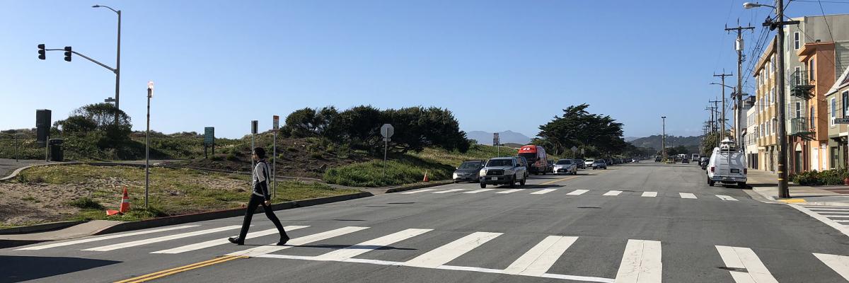 Lower Great Highway approaching Lawton Street, looking north. A pedestrian is crossing in the crosswalk.