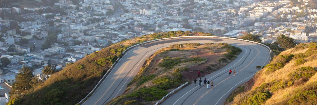 People walking up to Twin Peaks with the city skyline in the background