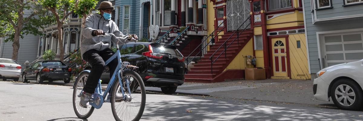 A person wearing a mask rides a bike along Shotwell Street