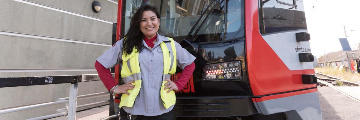 A smiling Muni operator in front of a new light rail vehicle