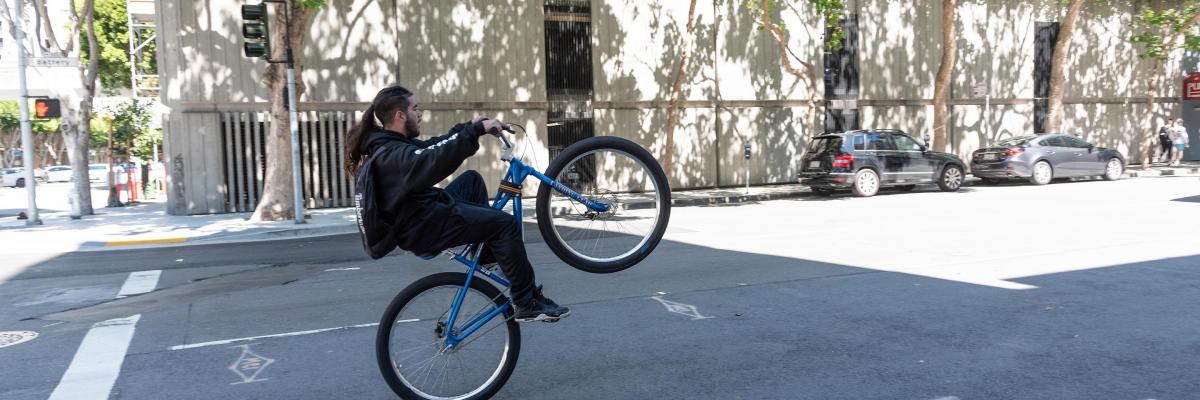 A person riding a bicycle on Battery Street raises the front wheel into the air