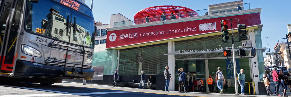 Street view outside the new Chinatown-Rose Pak station with a banner that says "Connecting Communities" and a bus approaching