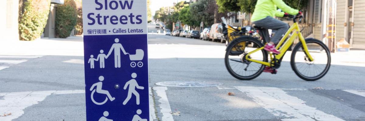 a person on a yellow bike passes by a Slow Streets program sign