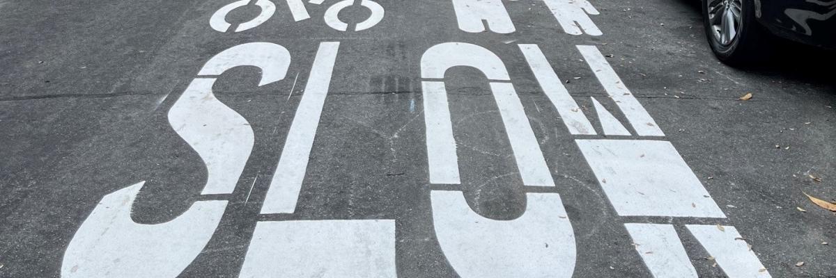 Slow Streets pavement markings in white show the outline of a cyclist, an adult and a child, and the word SLOW.