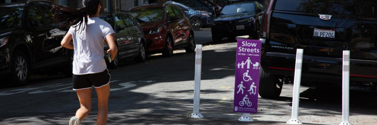 A person running past a purple Slow Streets program sign