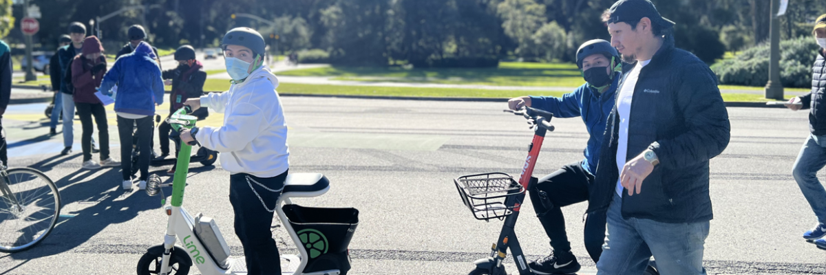 Two people riding adaptive scooters, one from Lime and one from Spin, in Golden Gate Park