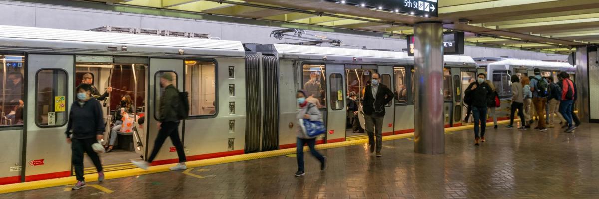 riders wearing masks walk on platform of powell muni metro station