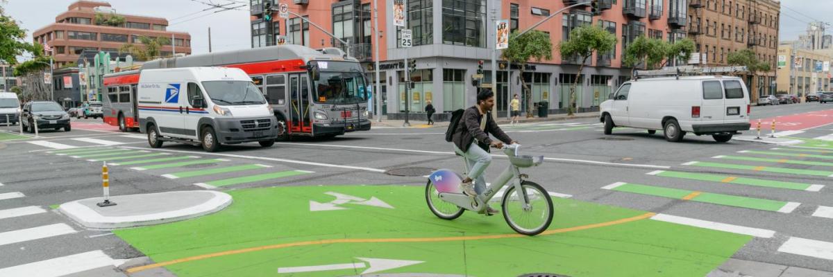cyclist using new protected bike facilities at the intersection of 3rd and Townsend. Muni bus driving in the intersection