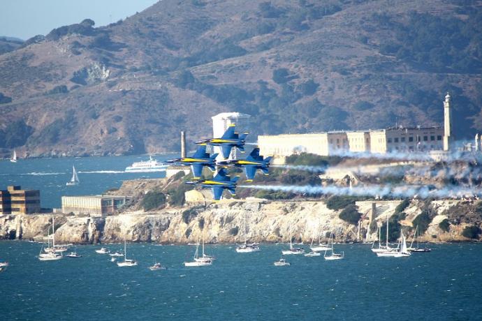 Blue Angels fighter jets in tight formation flying passed Alcatraz Island during the day.