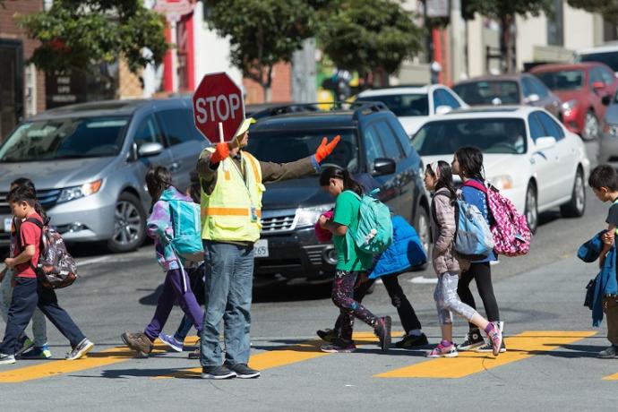 A crossing guard holds a stop sign as children walk in a crosswalk in front of stopped cars.