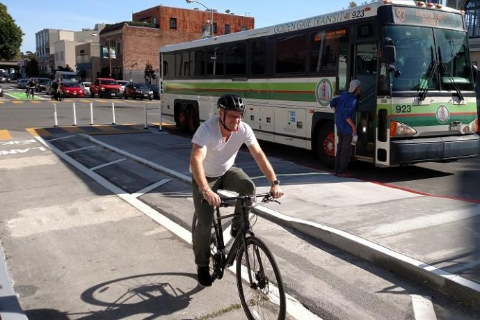 Man biking in a parking-protected bike lane and transit boarding island on 7th Street.