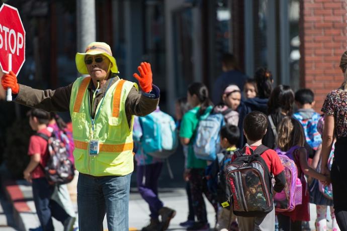 Crossing guard holding stop sign as students and parents cross the street.