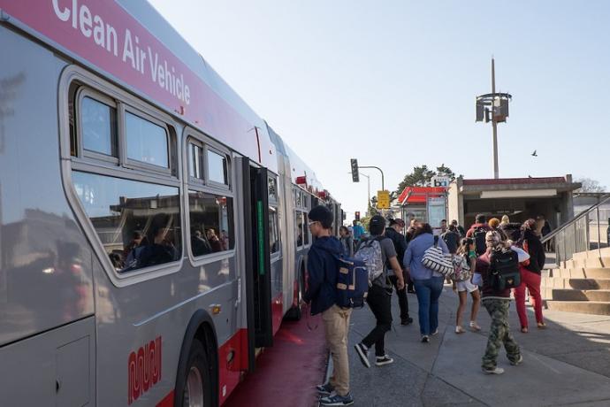 People board a Muni bus in front of Balboa Park Station.