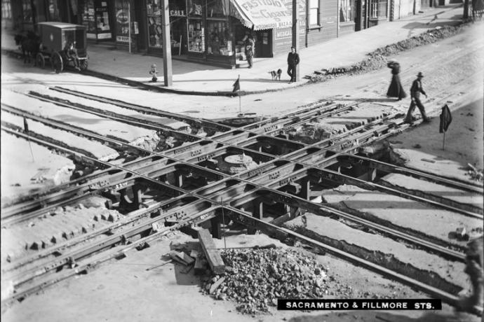 Overhead view from 1905 of Fillmore and Sacramento Streets.  Track construction occupies the intersection and a corner store with people around it is at top center.