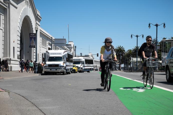 A person bicycling towards the camera in the green bike lane on the Embarcadero's roadway