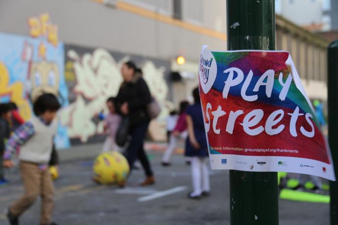 Play Streets event with colorful flyer in the foreground and children playing in the background