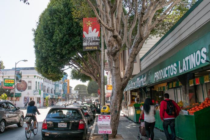 street scene in Mission district with produce market, people walking and cyclist