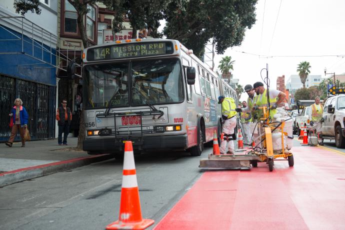 Crew placing red transit only lanes next to a 14R bus