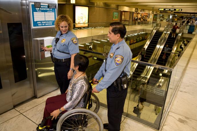 Image of two Muni safety officers helping a woman in a wheelchair into an elevator