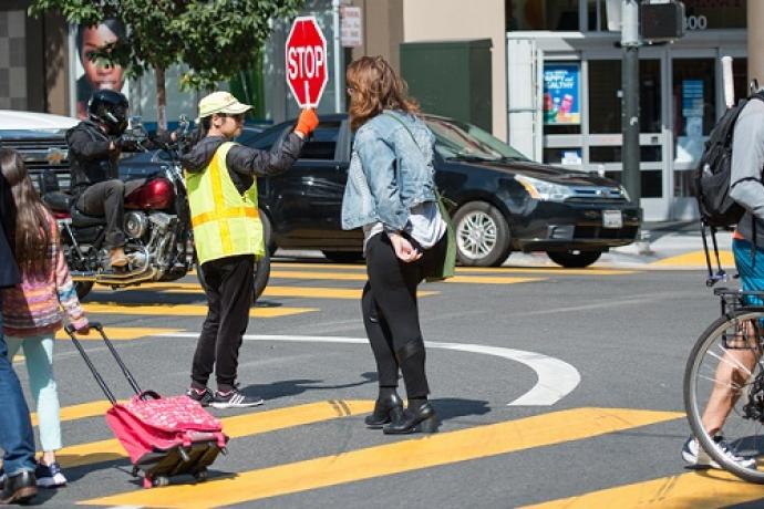 People crossing the street with the help of a crossing guard.