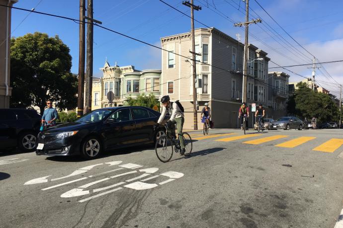 View of Page Street at Webster looking west. Eastbound cyclists are navigating around queued vehicle traffic.