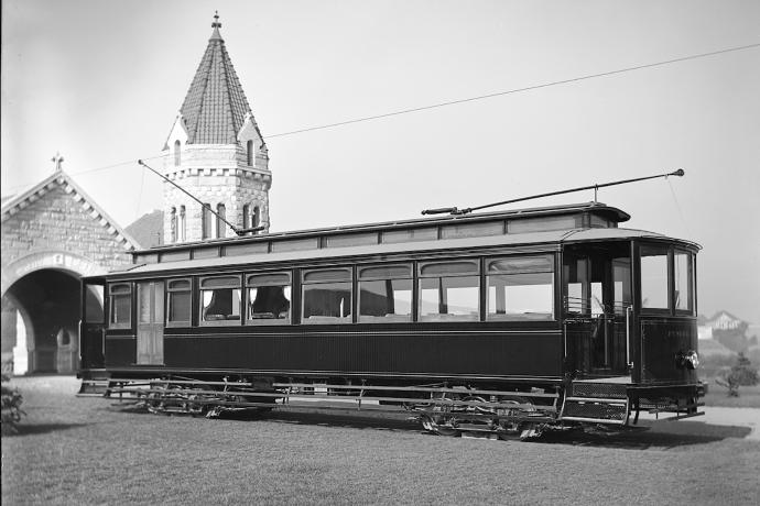 Funeral streetcar at cemetery with stone building in background