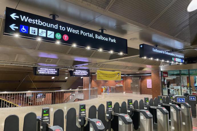 Photo of subway station fare gates with new overhead wayfinding signs depicting east, west directions and destinations for train