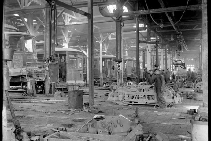 A view inside the overhaul shop in 1912 showing a row of streetcars at left and staff tearing down trucks and motors at right.