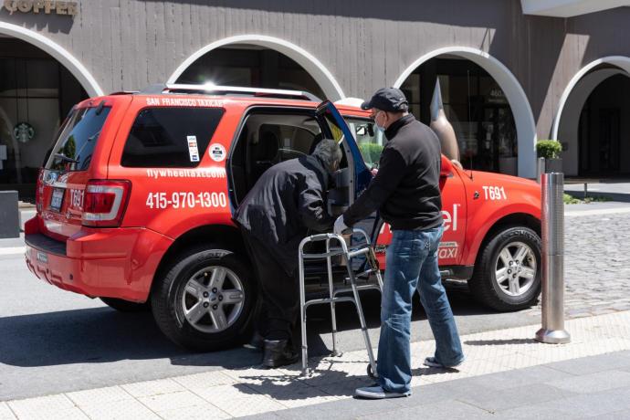 A taxi driver assists a passenger using a walker