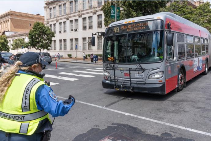 A traffic control officer guides a 49 Van Ness bus across an intersection