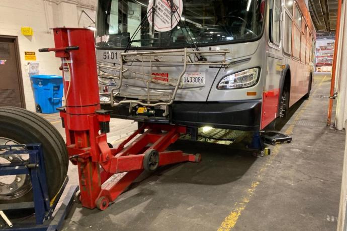 The front end of a trolley bus is hoisted of the ground by a red hydraulic jack