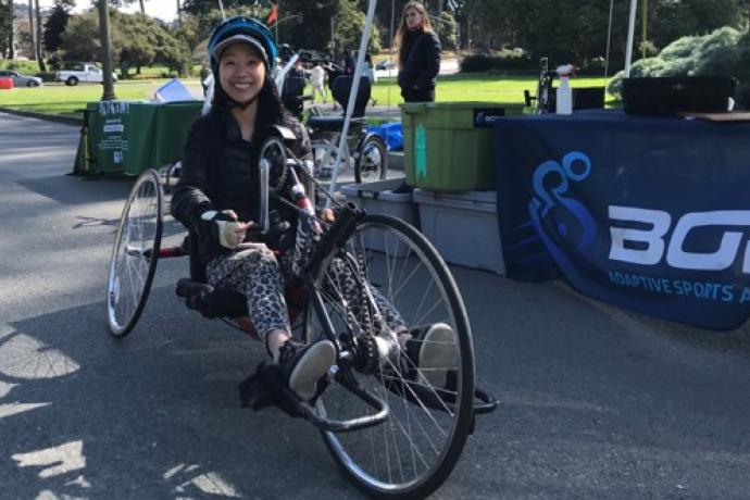 A woman sits on an adaptive recumbent bike in Golden Gate Park; a sign for BORP is in the background.