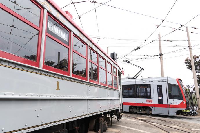 Muni streetcar 1 and new light rail vehicle in yard, both painted grey and red.