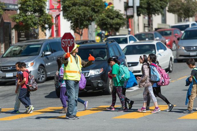 Crossing guard in the crosswalk holding a STOP sign with several children  walking 