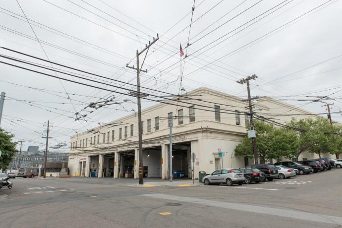 Bus yard entrance with parked cars along the building side up the hill 