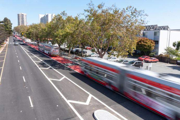 Blurred image of a bus traveling on a city street with trees in the media and building seen in the distant 