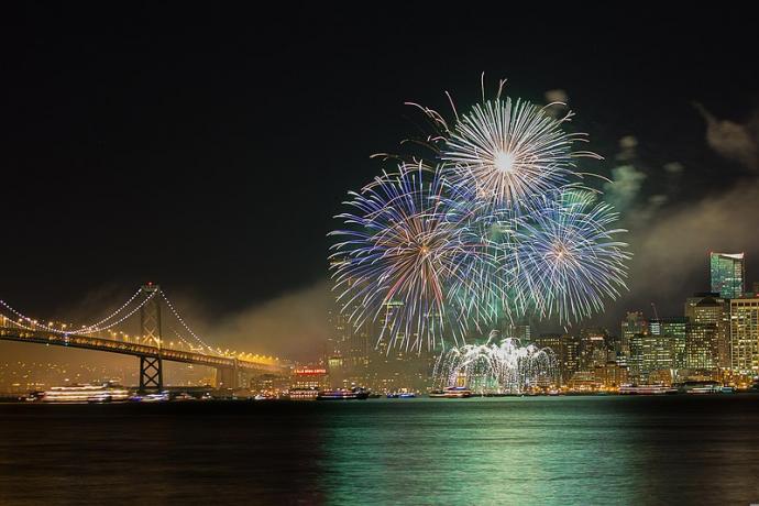 Fireworks over the the vary with a lighted city skyline and bridge in the background 