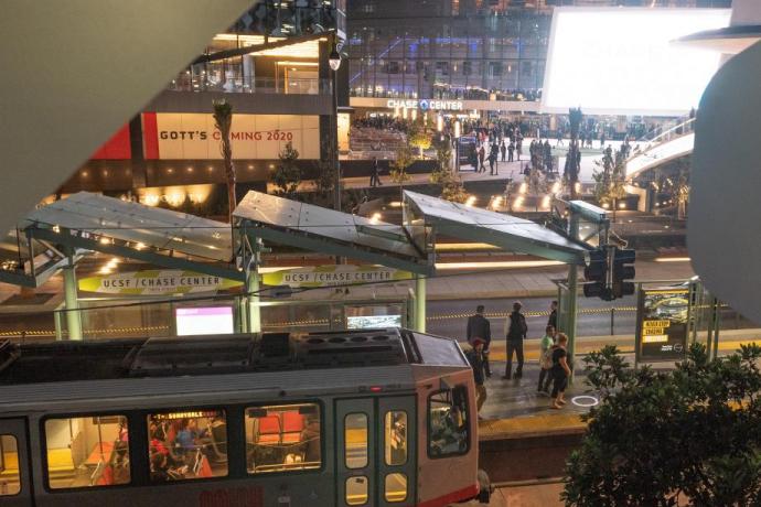  Photo of a Muni Metro train at the UCSF/Chase Center platform with Chase Center in the background.