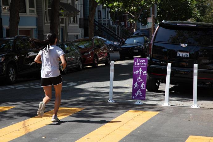 A person running on a Slow Street with a purple Slow Streets program sign