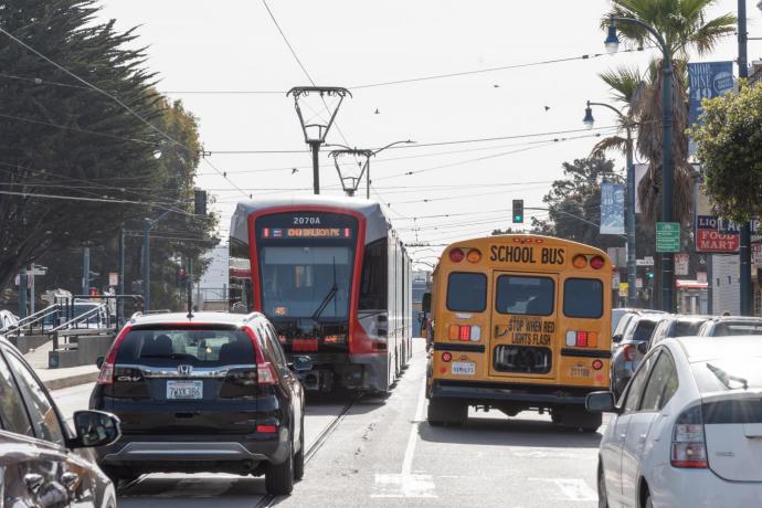 K Ingleside train running on Ocean Avenue as it crosses Faxon Avenue. Car traffic is present in front of and beh