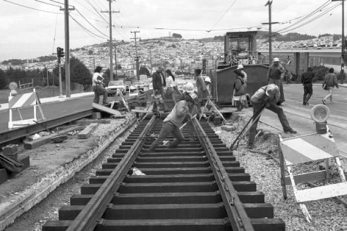 Group of people working on tracks, one pushes a rail while the other lifts a tie into place